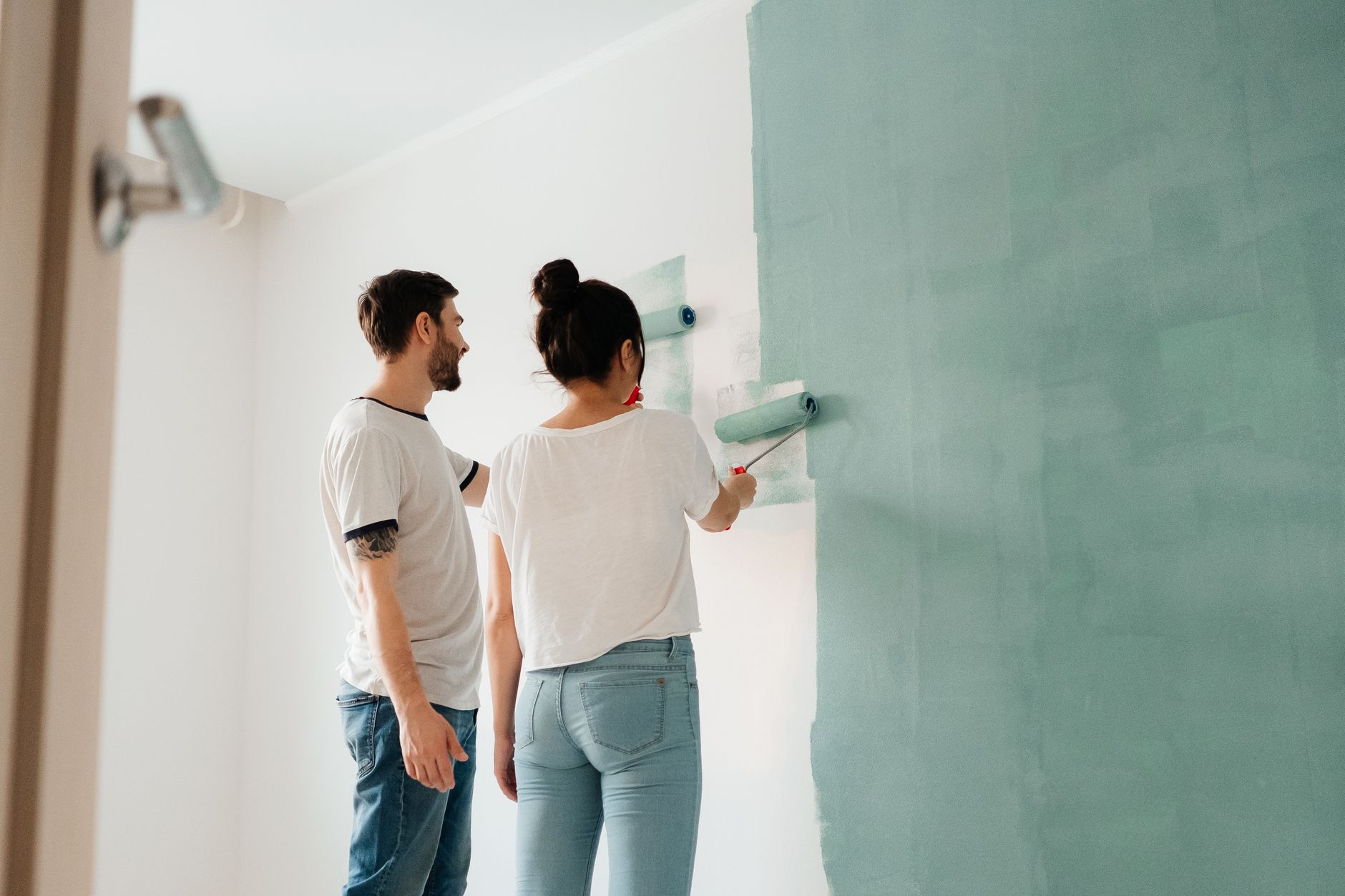 A couple collaborates to paint a wall with a roller indoors, showcasing teamwork in Long Beach, CA